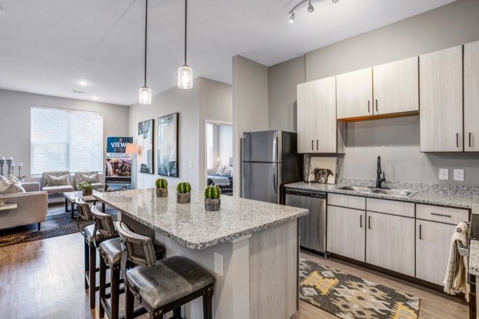 An apartment at Views of Music City featuring an open kitchen with a granite countertop island, stainless steel appliances, and a large living room nearby. 